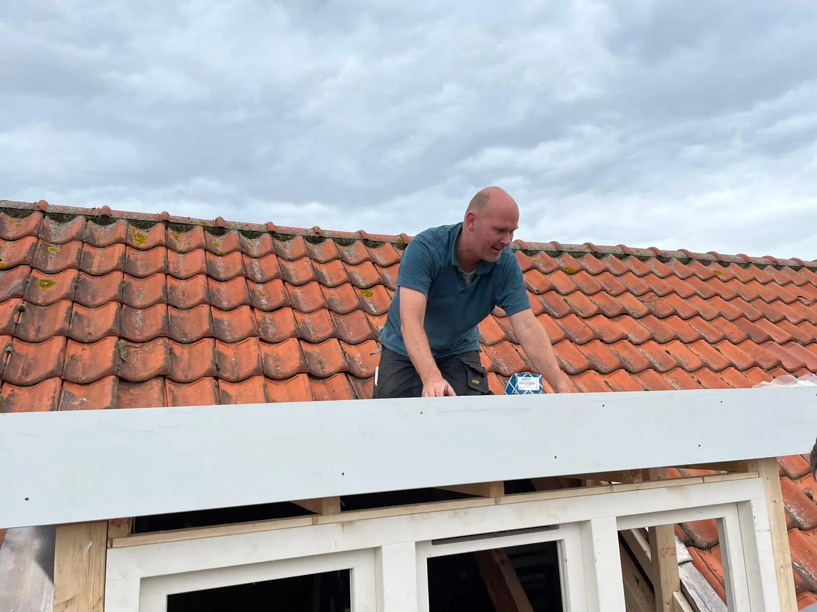Vakman plaatst een dakkapel en werkt aan de witte boeiboord op een pannendak