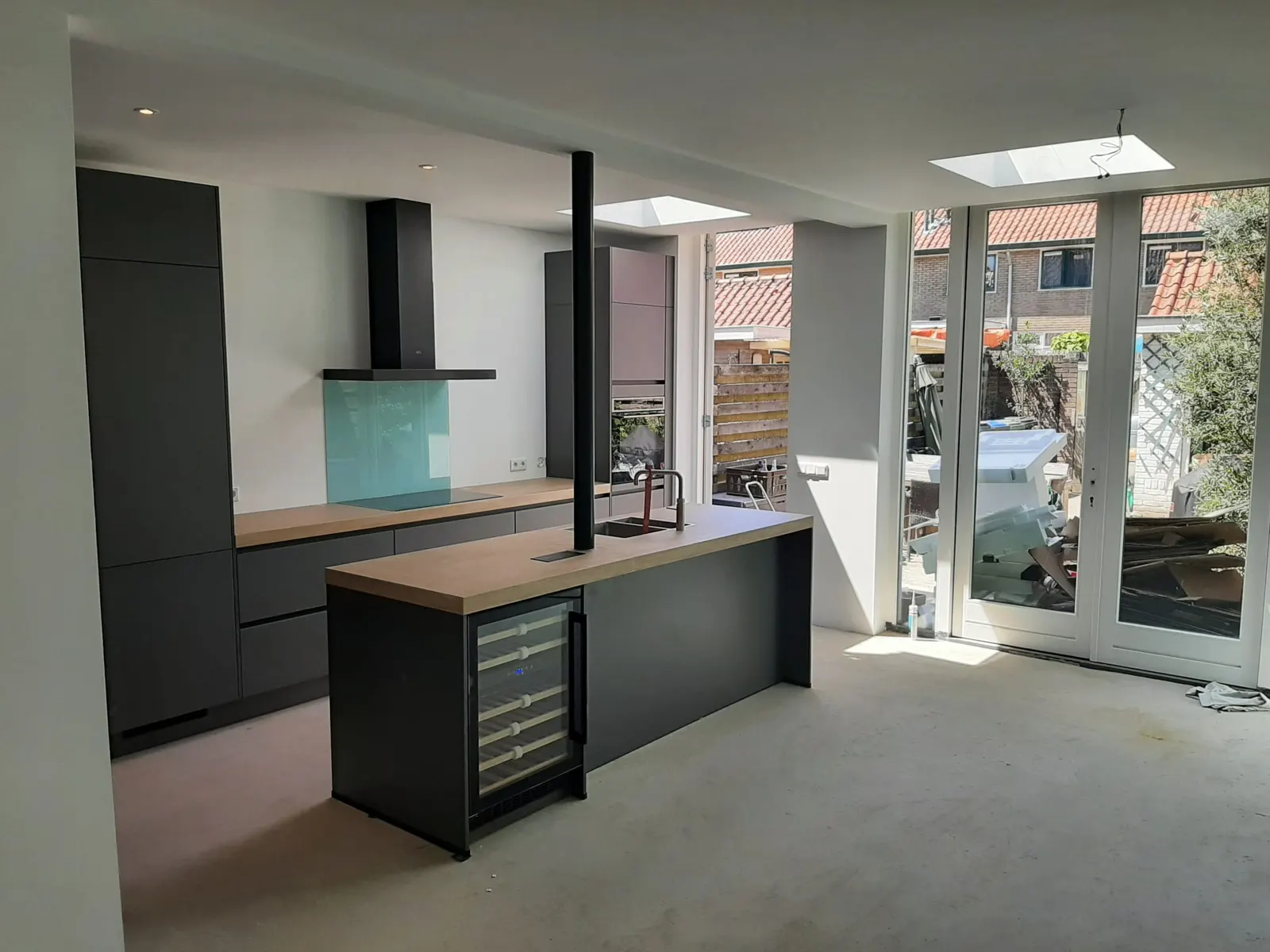 Lichte keuken met kookeiland, houten blad en grote puien naar de tuin
