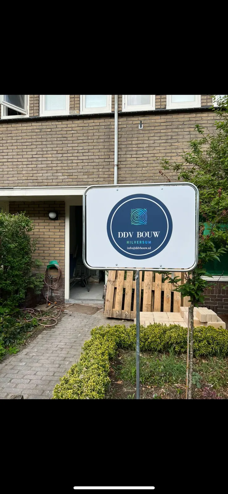 Bouwbord van DDV Bouw in een voortuin, met de vermelding Hilversum