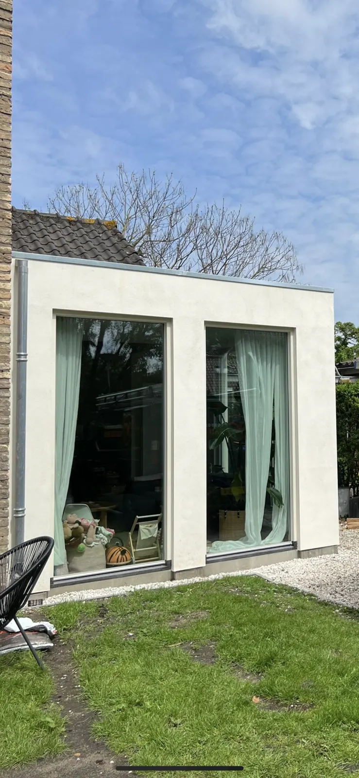 Kleine lichte aanbouw met glaspuien tegen de zijgevel van een woning