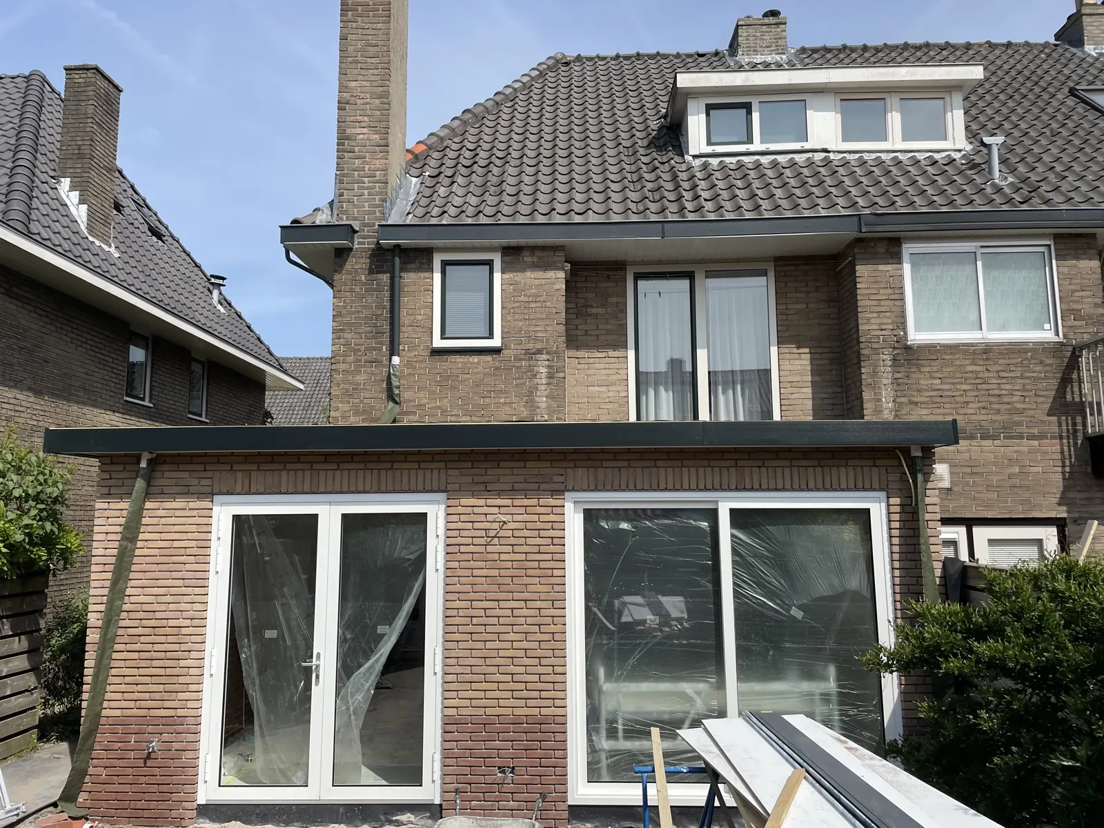 Gemetselde uitbouw met plat dak aan een bakstenen woning, met nieuwe kozijnen