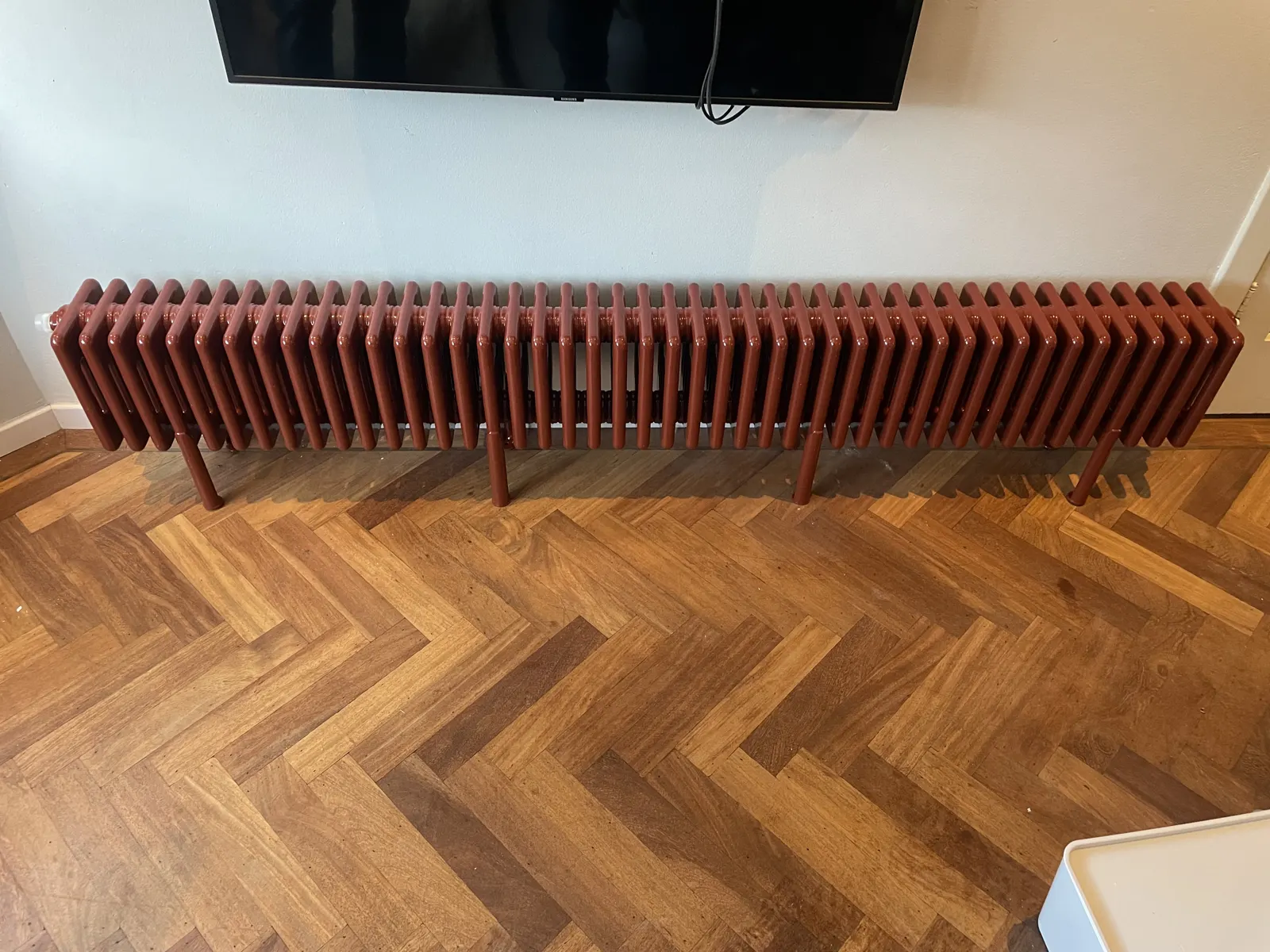 Rode kolomradiator tegen een wand, op een visgraat eiken vloer