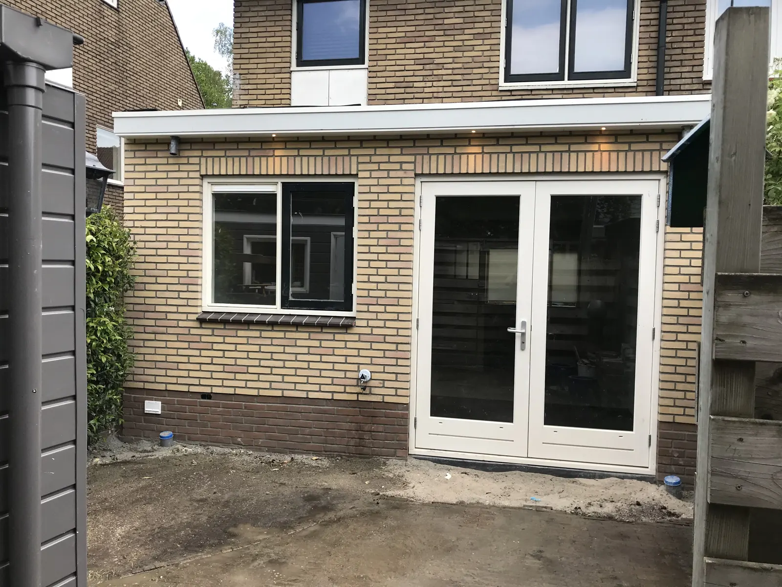 Nieuwe aanbouw in gele baksteen met witte tuindeuren