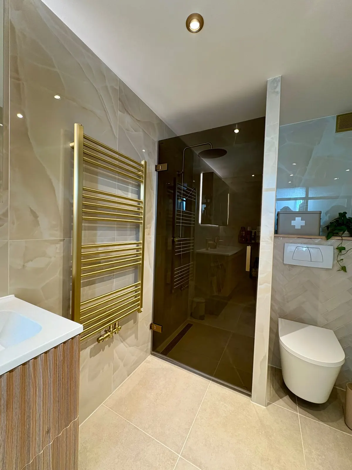 Overzicht van een luxe badkamer met gouden radiator, glazen douche en hangend toilet