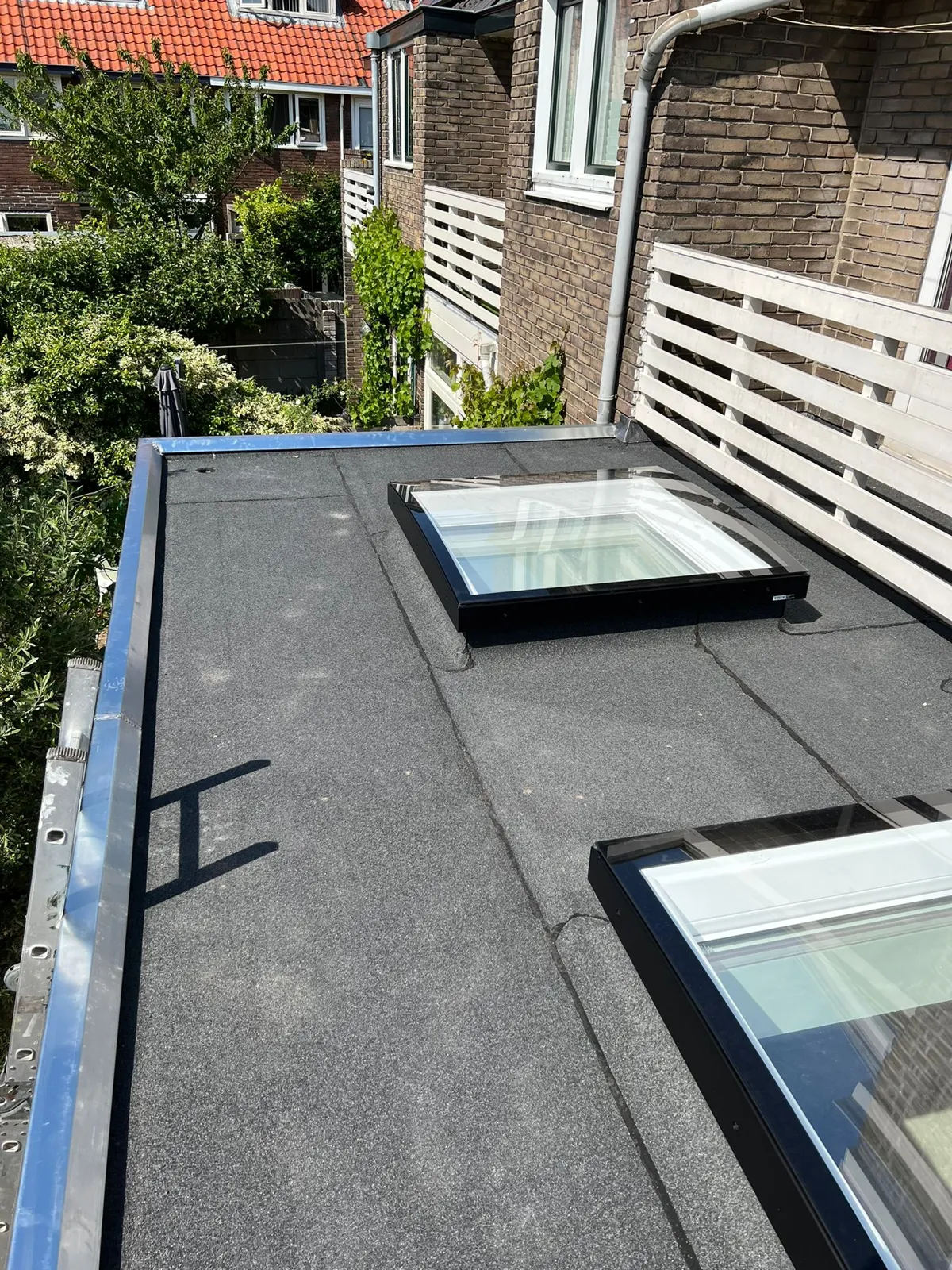 Plat dak met donkere bedekking en twee lichtkoepels
