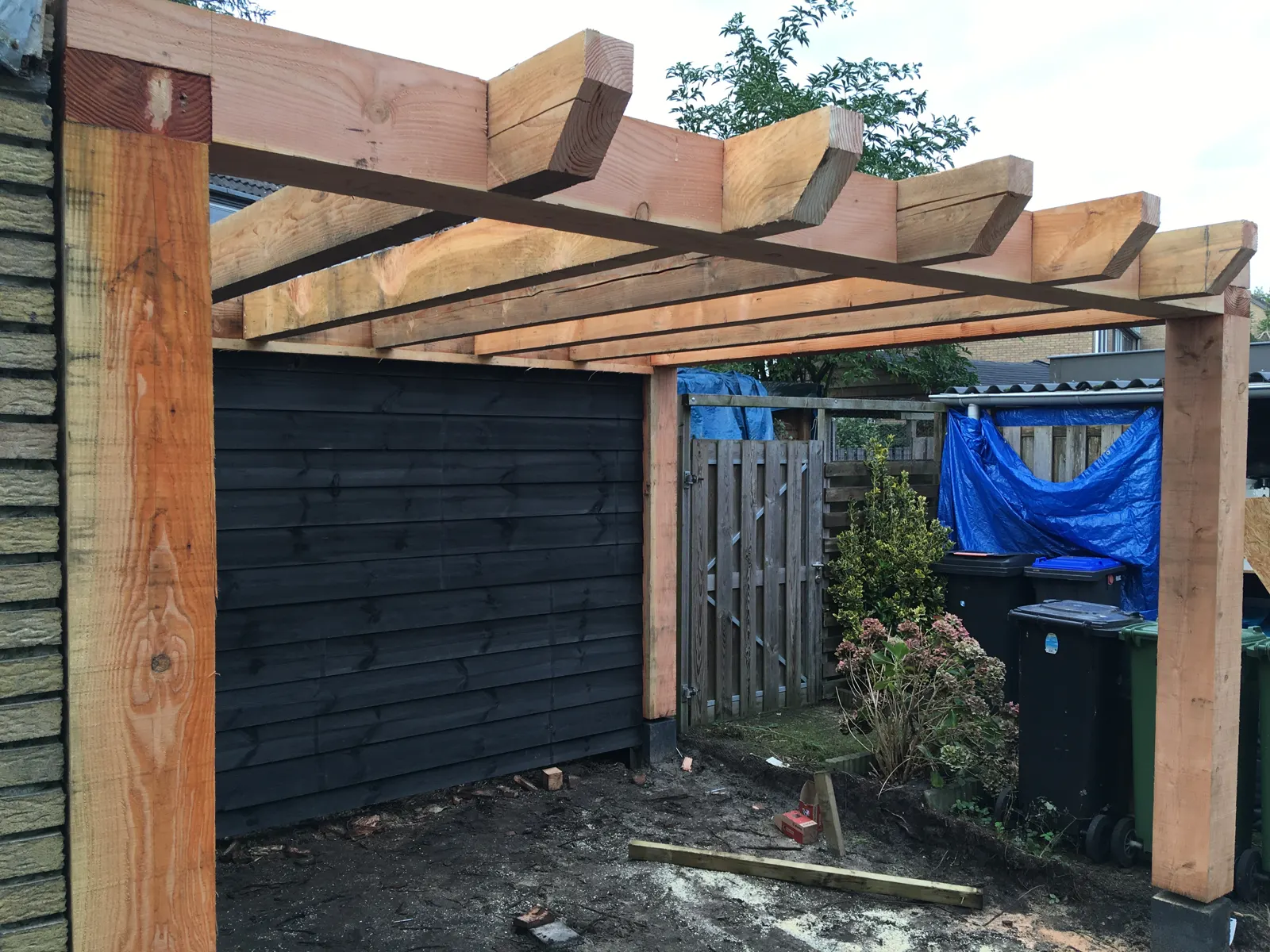 Houten pergola in aanbouw tegen een donkere schutting